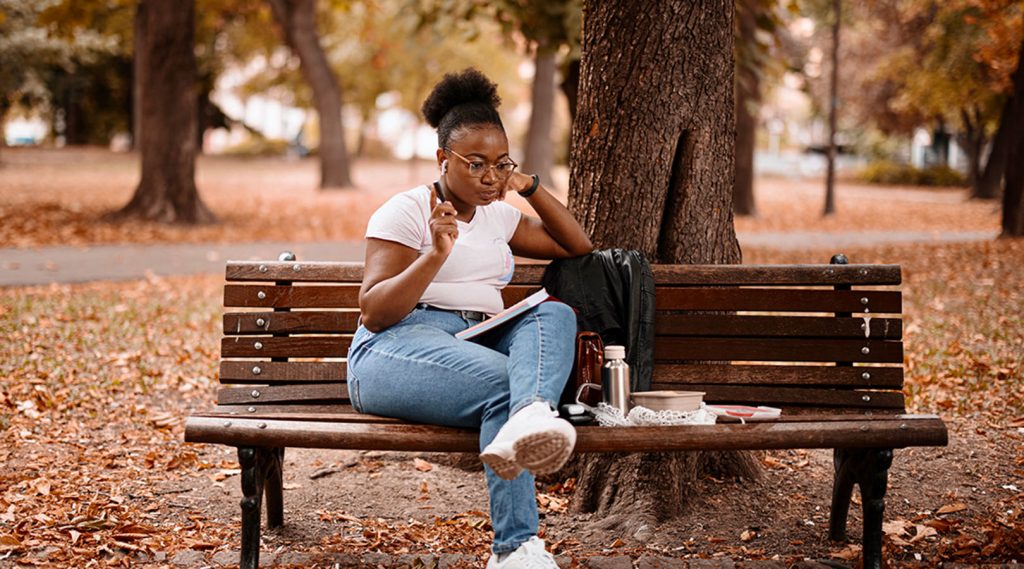 Un jeune adulte assis sur un banc dehors avec un carnet